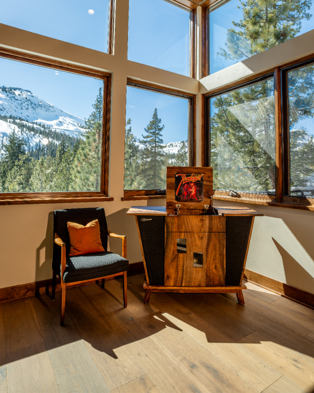 Streamline HiFi stereo console in living room with many windows and a beautiful snow-covered mountain view through the windows - sun beaming in.