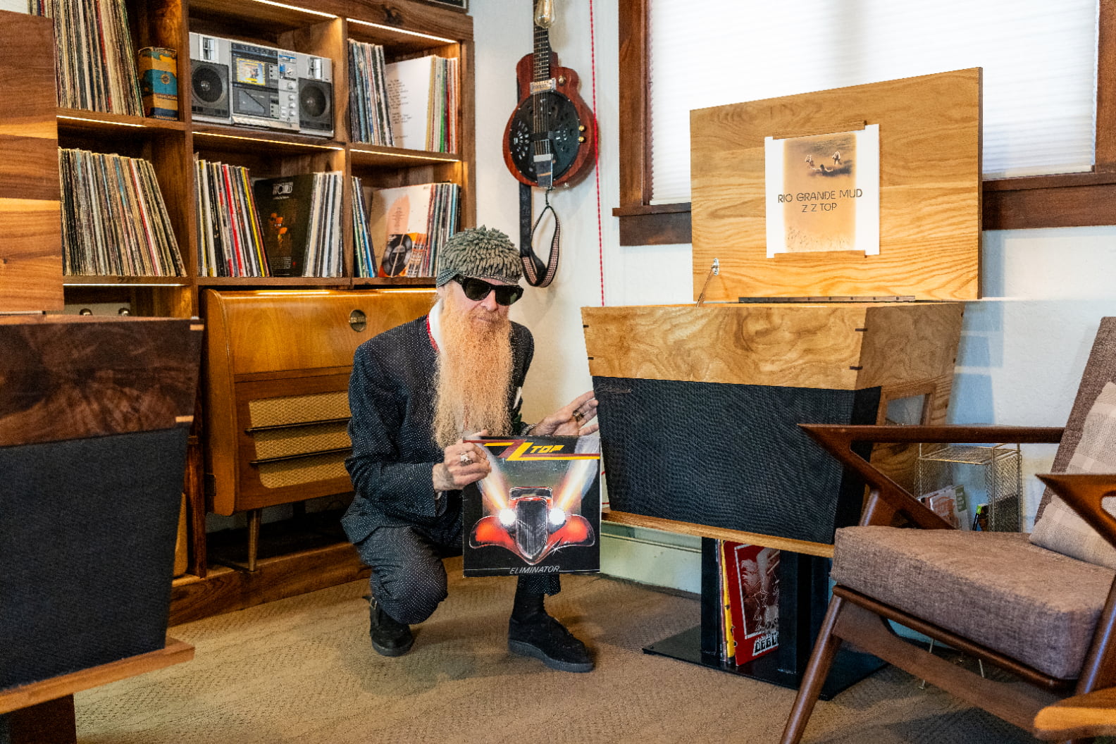 Billy Gibbons squatting in front of Streamline HiFi stereo console cabinet holding a ZZ-Top record as an expression of endorsement of Streamline HiFi.